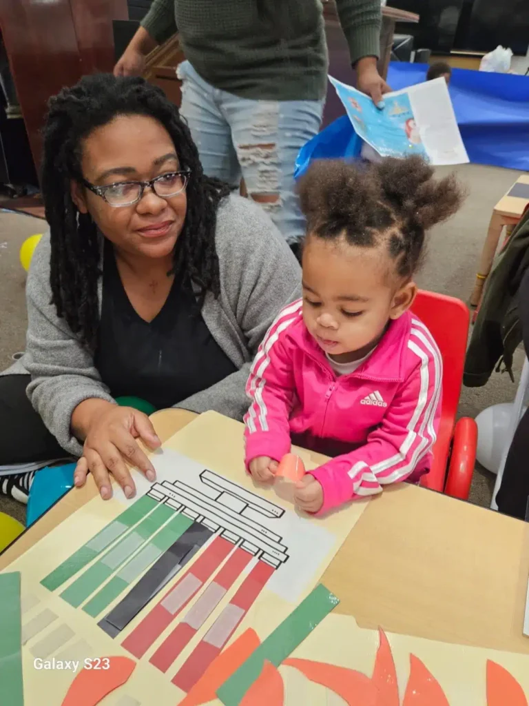An Early Childhood educator assisting a young child with her crafts.