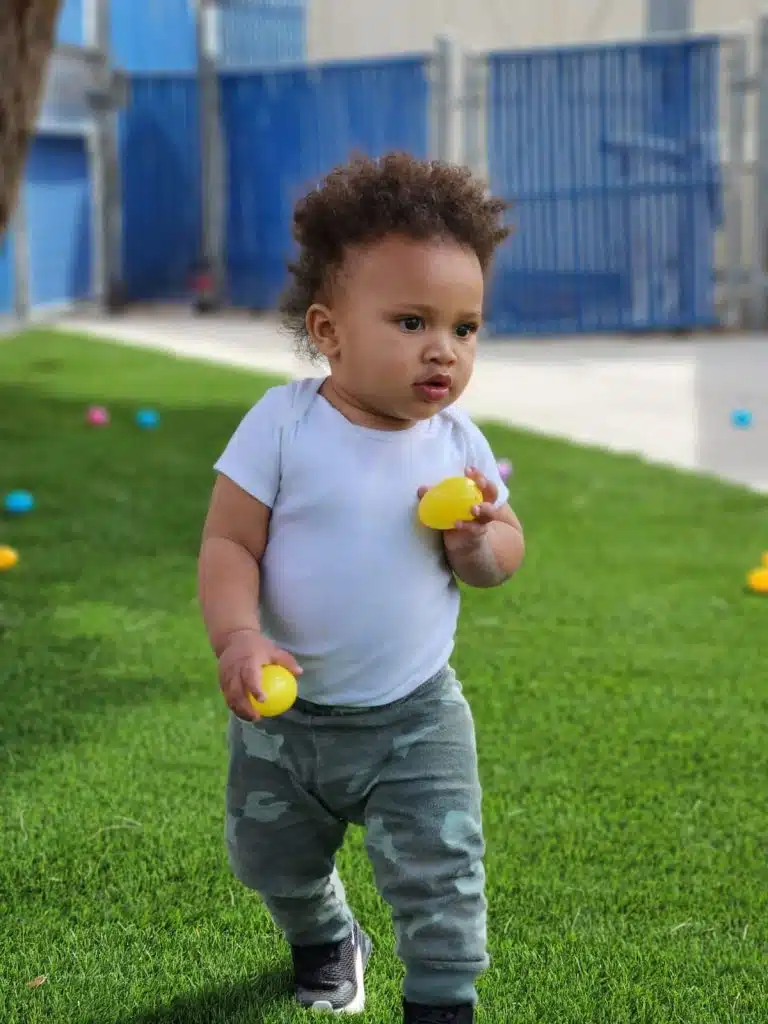 infant boy walking around collecting plastic eggs