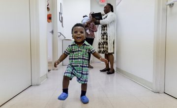Smiling toddler walking confidently in a supportive environment, highlighting the impact of early childhood education programs on development.