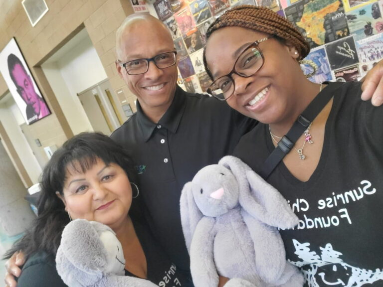 Two female teachers stand with a male teacher from Sunrise Children’s Foundation.