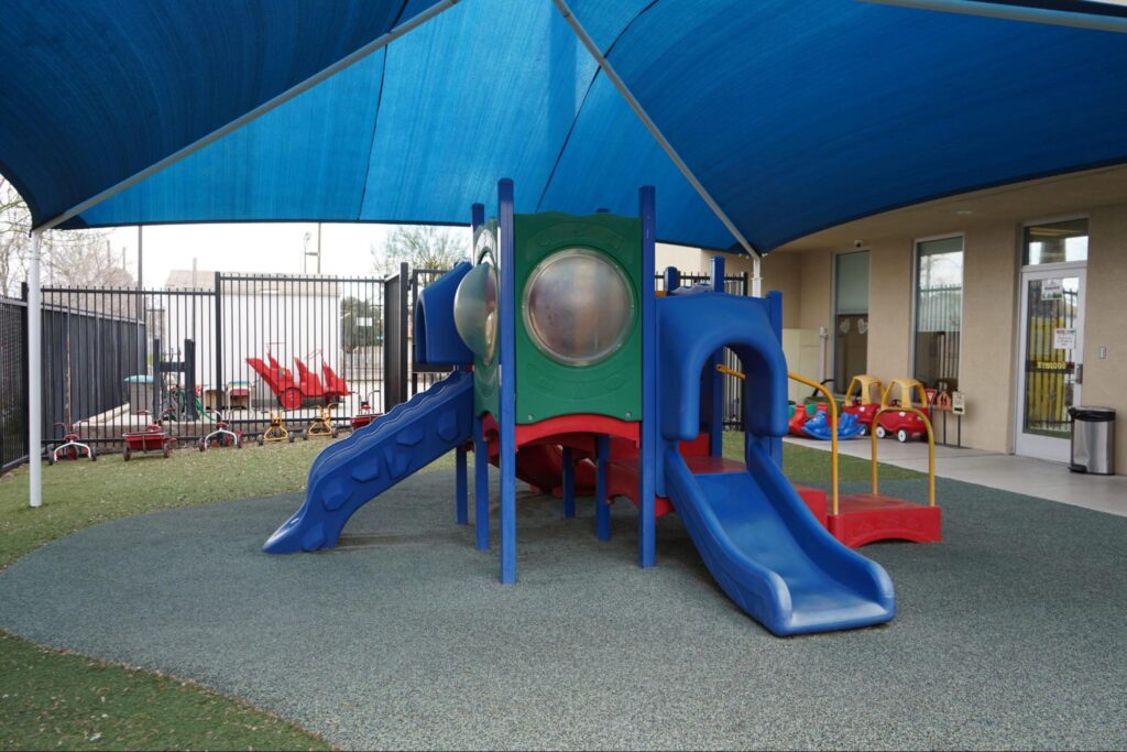 Playground with blue and red slides under a shade canopy at Spring Valley Early Head Start Programs